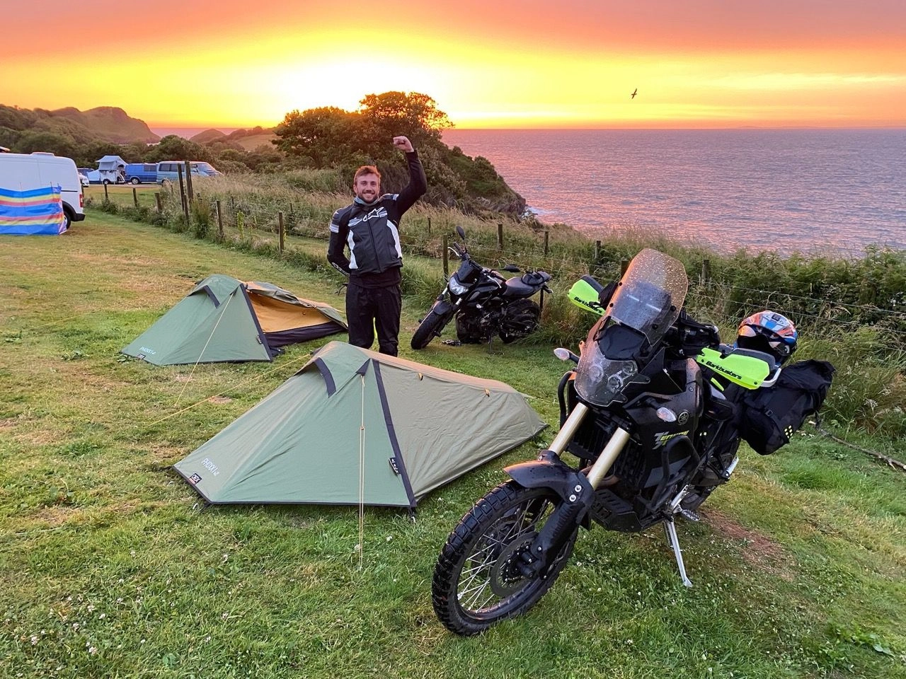 Zac celebrating a successful tent pitch, infront of a golden sunset, in Devon.